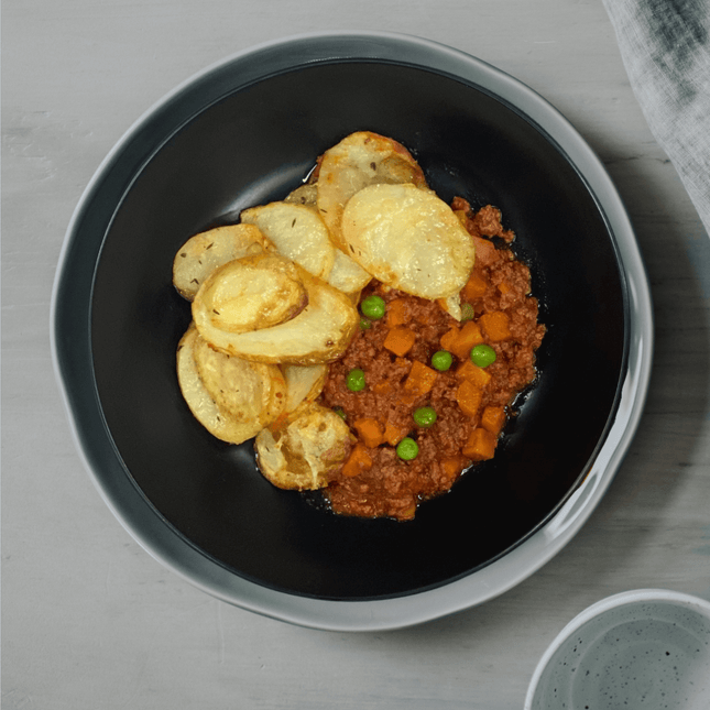Beef Cottage Pie Topped w/ Chat Potatoes & Mozzarella Cheese in a black bowl. This meal is Low FODMAP and gluten free
